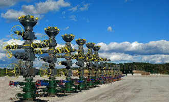 A row of frac stacks is shown against a blue sky and trees in the background.